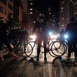 Protesters with bicycles stand with lights from police cars shining through